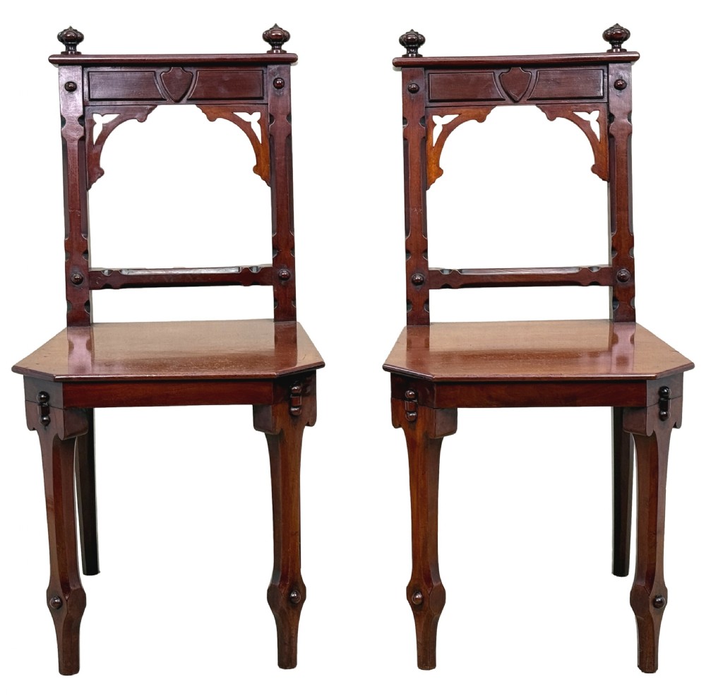 A pair of Victorian mahogany hall chairs featuring carved shield backrests, open architectural arches, turned finials, and solid wooden seats. View XIII