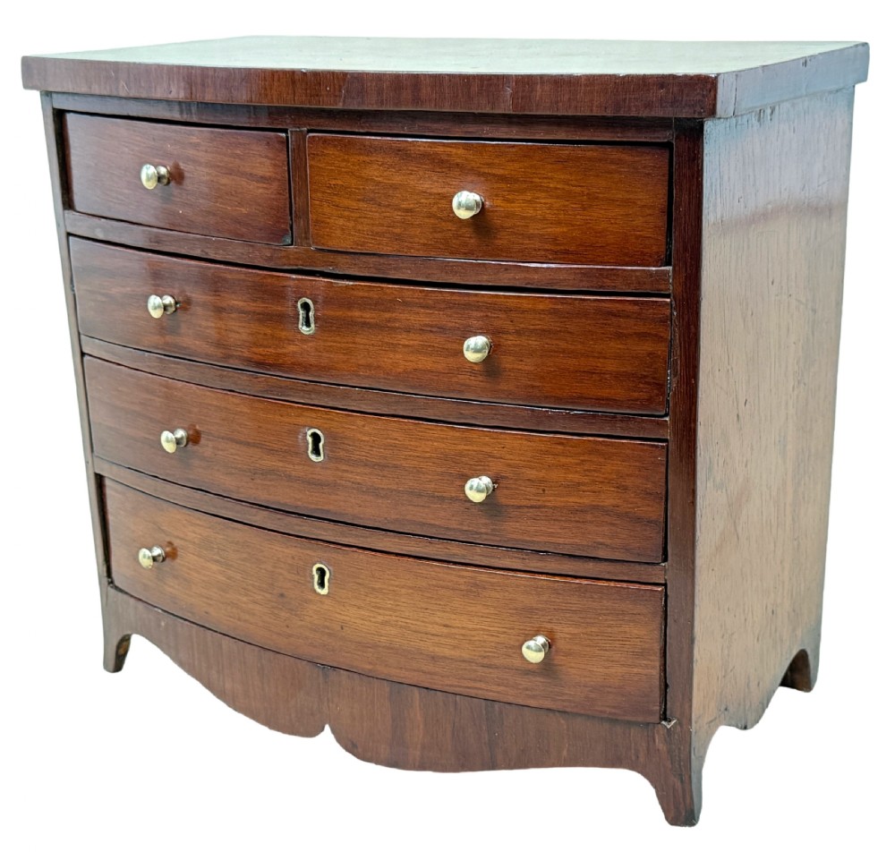 A 19th-century Victorian miniature mahogany bowfront chest featuring two short over three long graduated drawers with brass knobs and keyholes. View IV