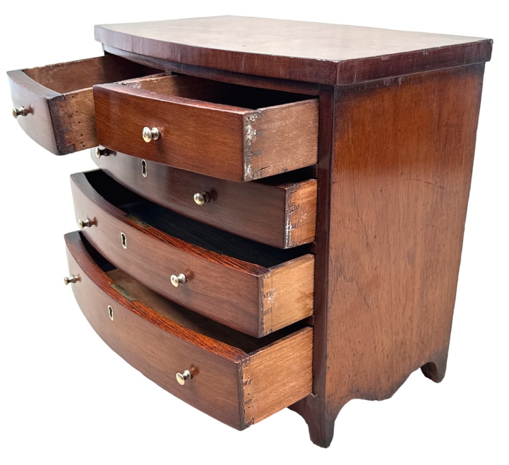 A 19th-century Victorian miniature mahogany bowfront chest featuring two short over three long graduated drawers with brass knobs and keyholes. View V