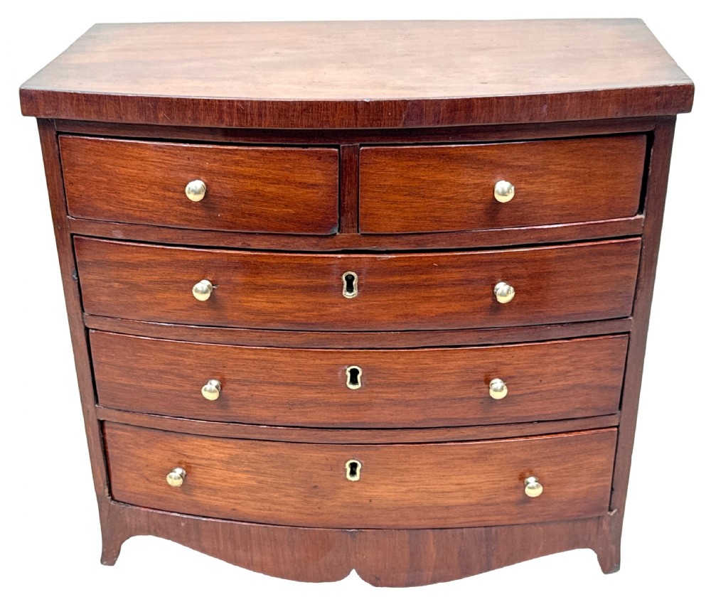 A 19th-century Victorian miniature mahogany bowfront chest featuring two short over three long graduated drawers with brass knobs and keyholes. View IX