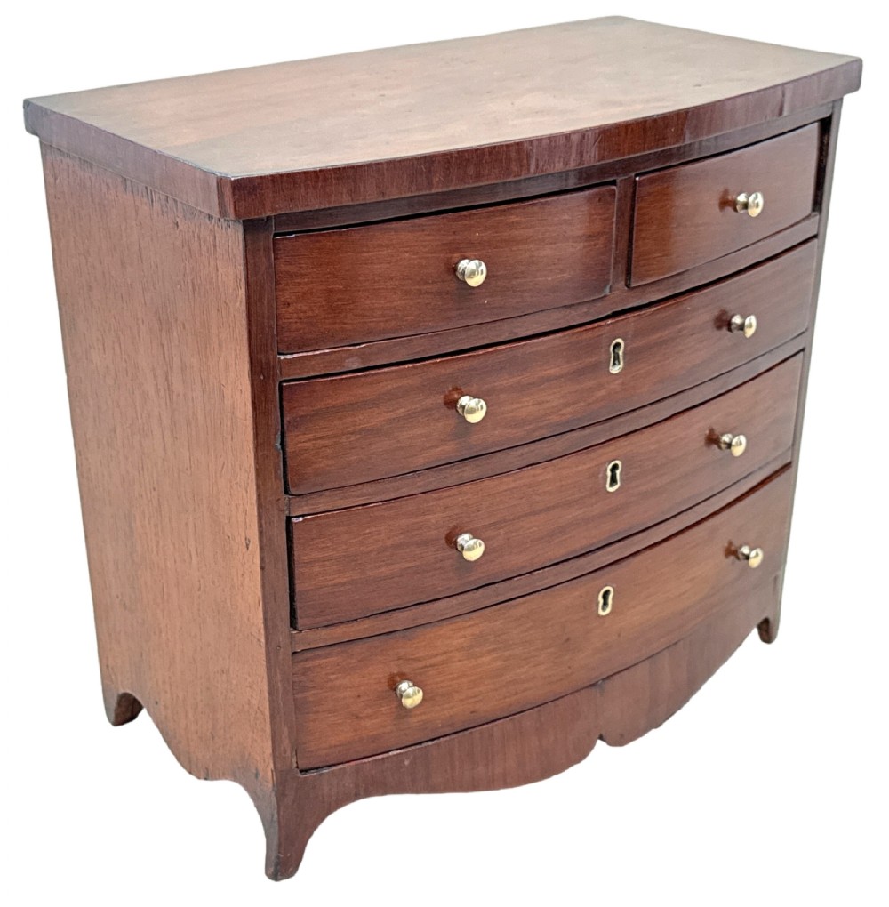 A 19th-century Victorian miniature mahogany bowfront chest featuring two short over three long graduated drawers with brass knobs and keyholes. View X