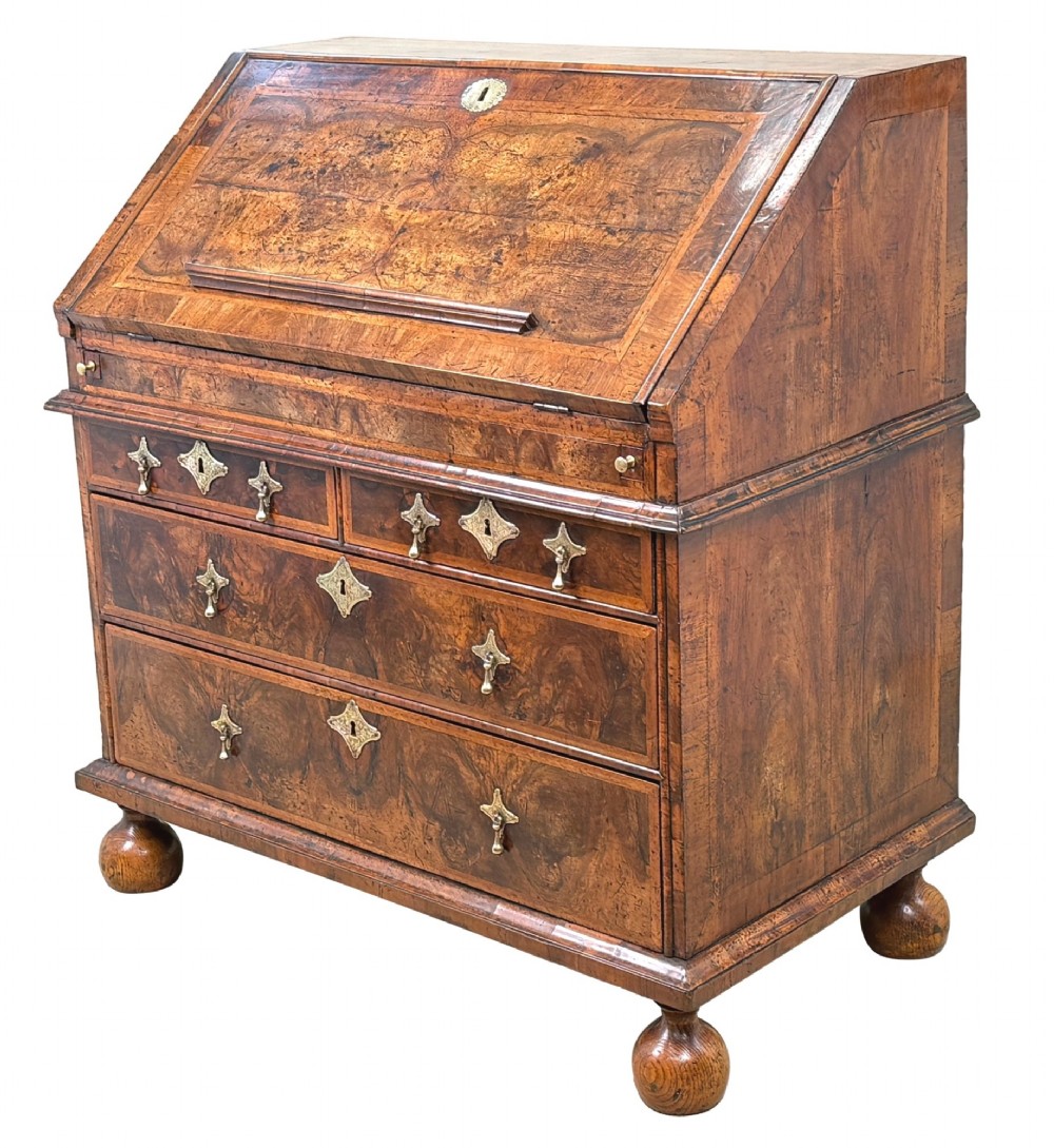 An early 18th-century Queen Anne walnut bureau featuring a slanted fall-front writing flap, brass escutcheons with drop handles, and turned bun feet.