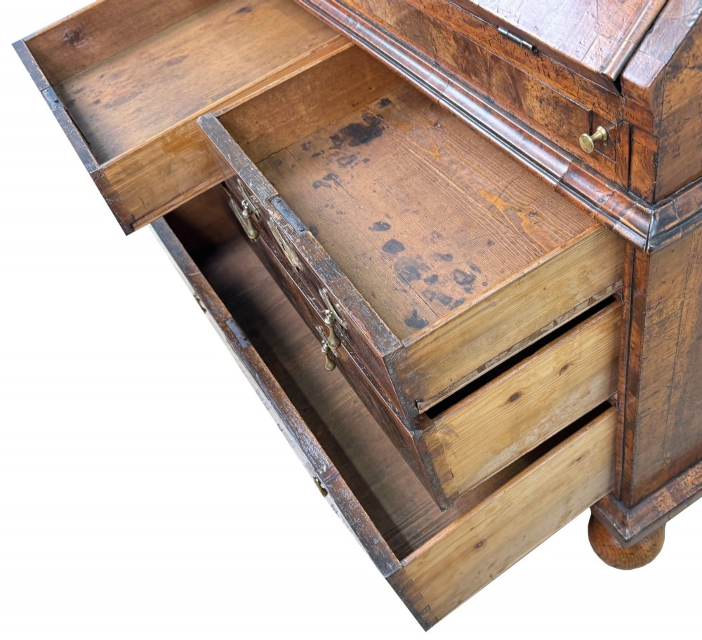 An early 18th-century Queen Anne walnut bureau featuring a slanted fall-front writing flap, brass escutcheons with drop handles, and turned bun feet. View VII