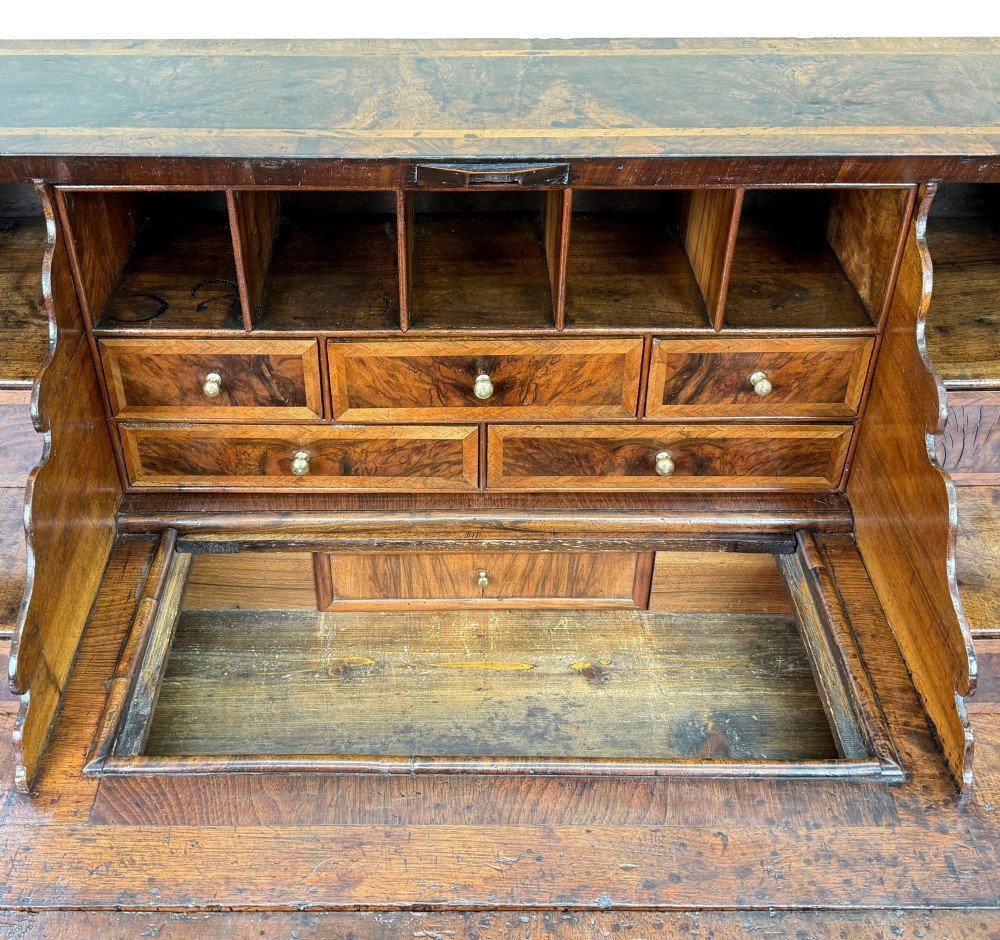 An early 18th-century Queen Anne walnut bureau featuring a slanted fall-front writing flap, brass escutcheons with drop handles, and turned bun feet. View XII