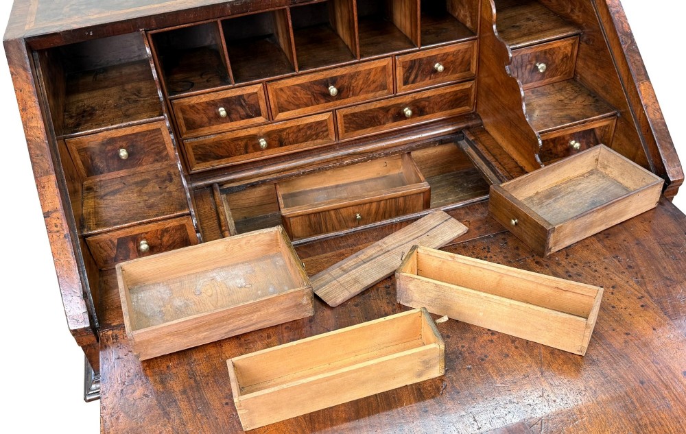 An early 18th-century Queen Anne walnut bureau featuring a slanted fall-front writing flap, brass escutcheons with drop handles, and turned bun feet. View XIII