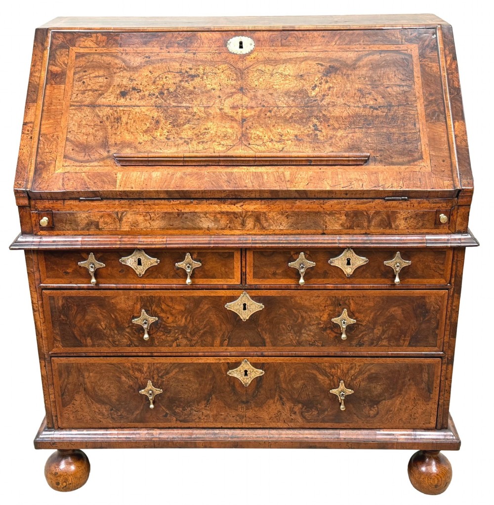 An early 18th-century Queen Anne walnut bureau featuring a slanted fall-front writing flap, brass escutcheons with drop handles, and turned bun feet. View XV