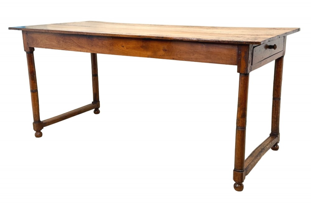 A 19th-century French Provincial fruitwood farmhouse table featuring a rectangular plank top, single end drawer, turned legs, and lower side stretchers.