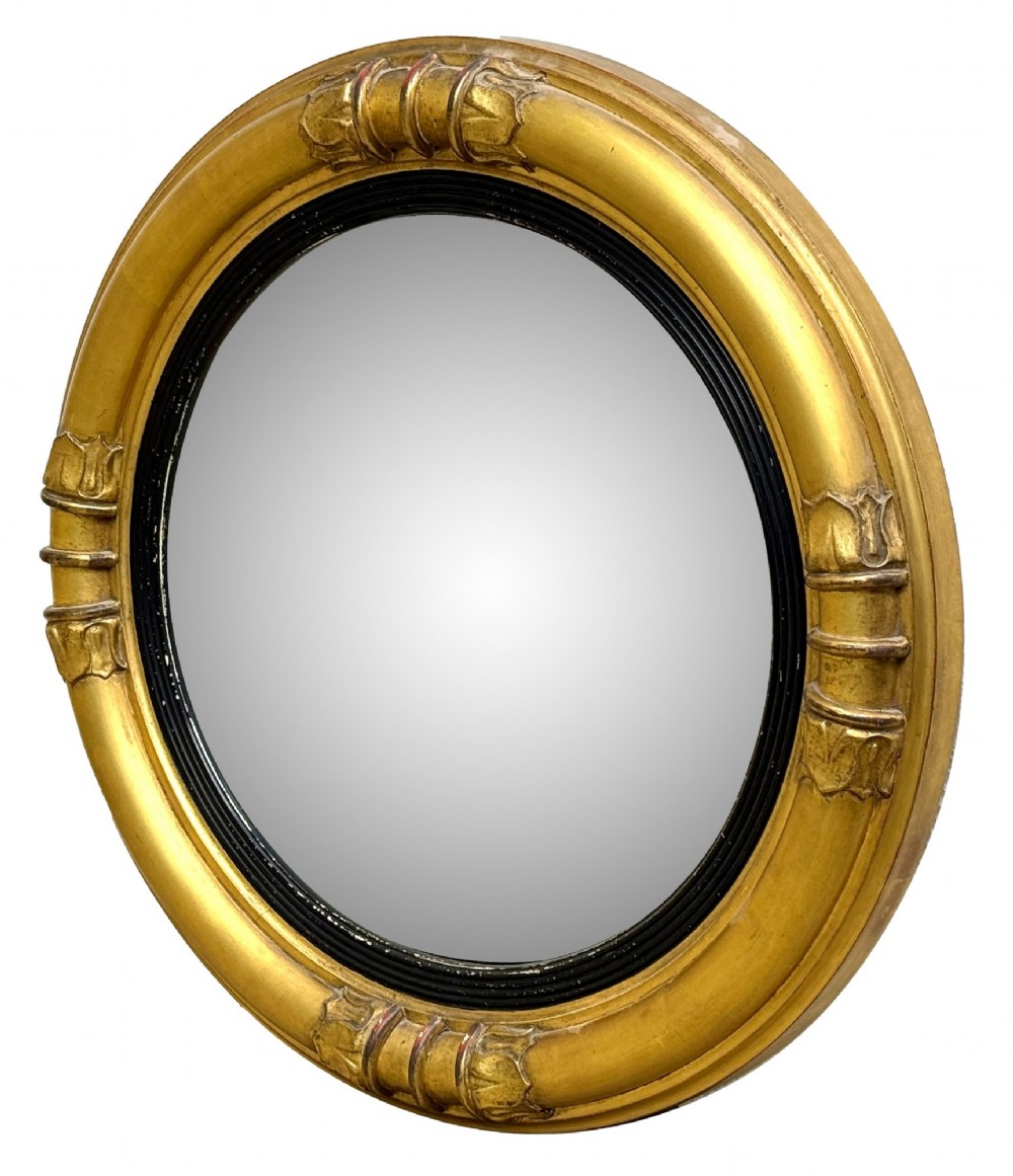 A mid-19th century circular convex mirror featuring a moulded giltwood frame with carved leaf clasps and an inner ebonised reeded slip.