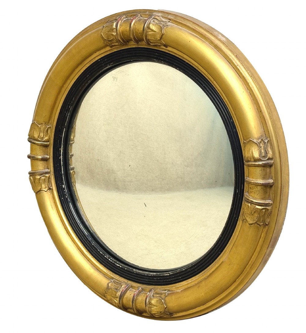 A mid-19th century circular convex mirror featuring a moulded giltwood frame with carved leaf clasps and an inner ebonised reeded slip. View II