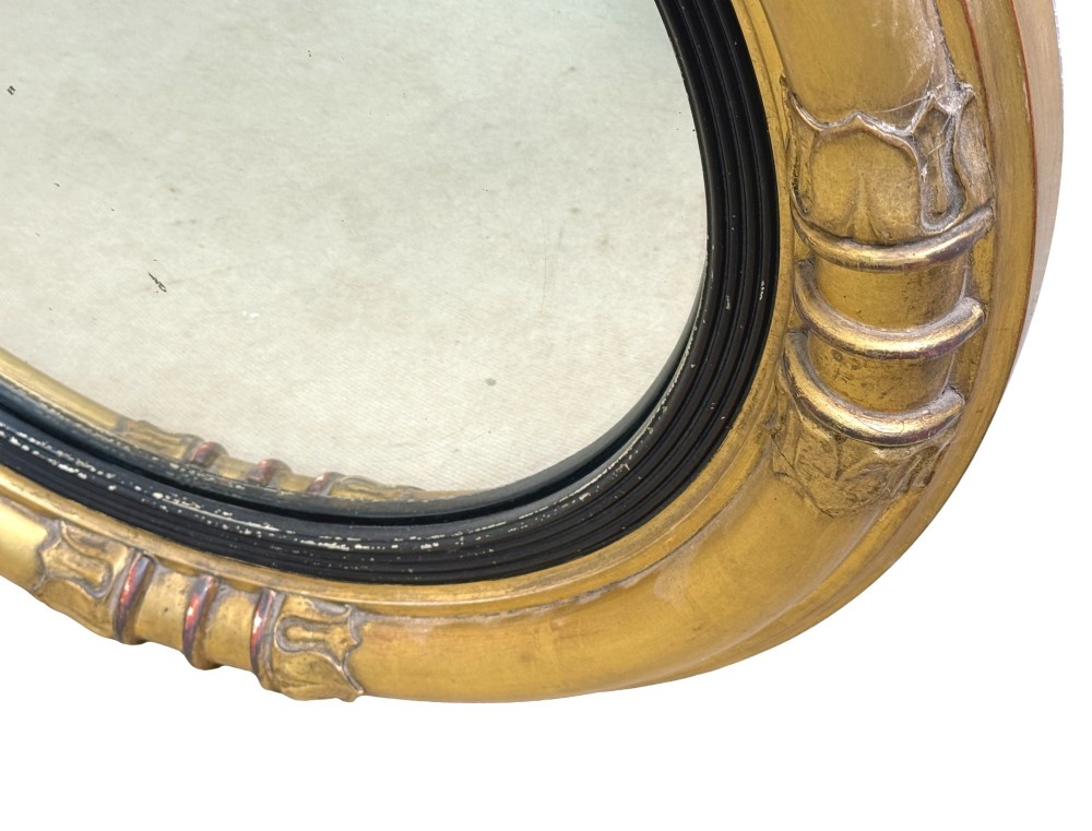 A mid-19th century circular convex mirror featuring a moulded giltwood frame with carved leaf clasps and an inner ebonised reeded slip. View V