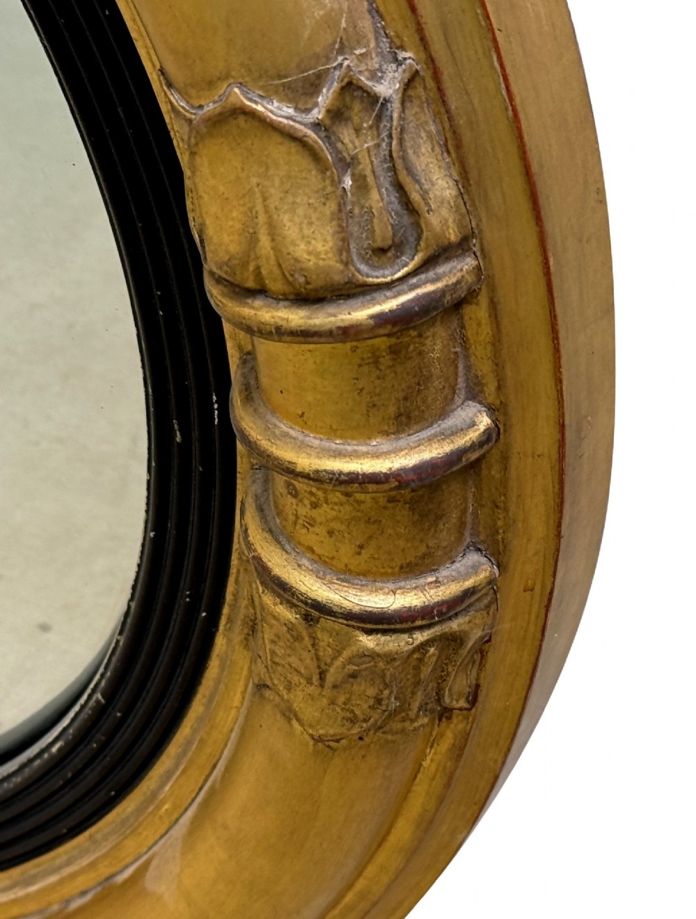 A mid-19th century circular convex mirror featuring a moulded giltwood frame with carved leaf clasps and an inner ebonised reeded slip. View VI