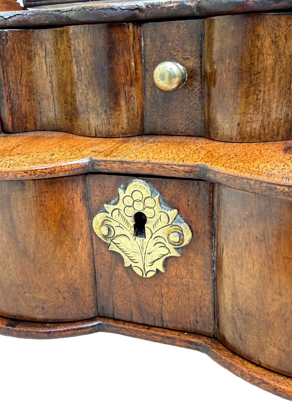 A Queen Anne early 18th-century walnut dressing table mirror featuring an arched swing frame resting above a stepped serpentine base with small drawers and brass hardware. View IX