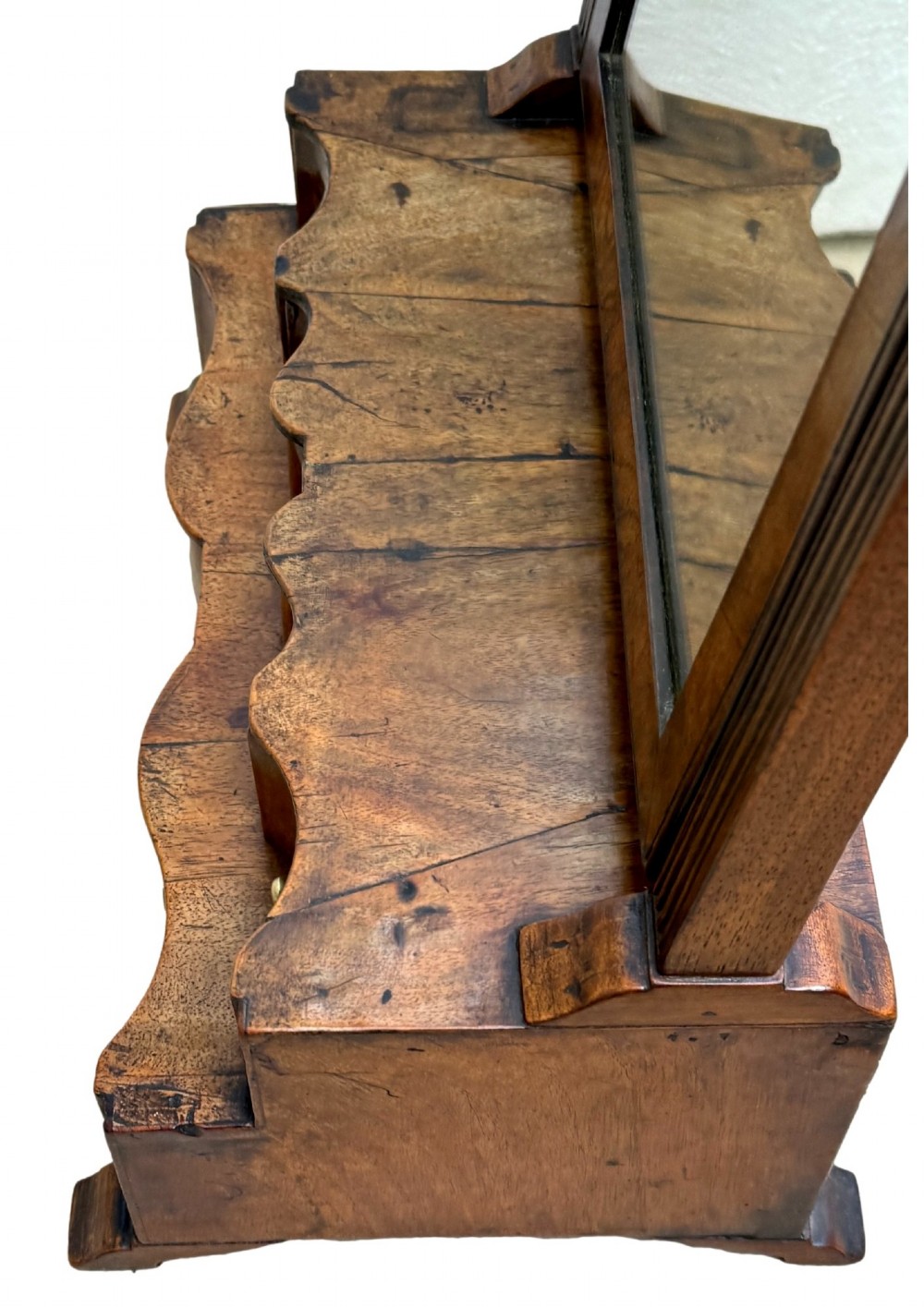 A Queen Anne early 18th-century walnut dressing table mirror featuring an arched swing frame resting above a stepped serpentine base with small drawers and brass hardware. View XI