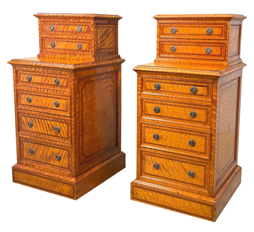A pair of 19th-century golden satinwood bedside chests featuring stepped top sections with drawers, crossbanded inlay, and brass ring handles.