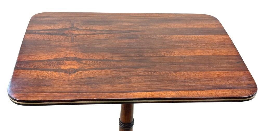 A nineteenth-century Regency rosewood occasional table featuring a rectangular top with rounded corners, fine brass inlay stringing, a turned central column, and a tripod base resting on brass feet. View II