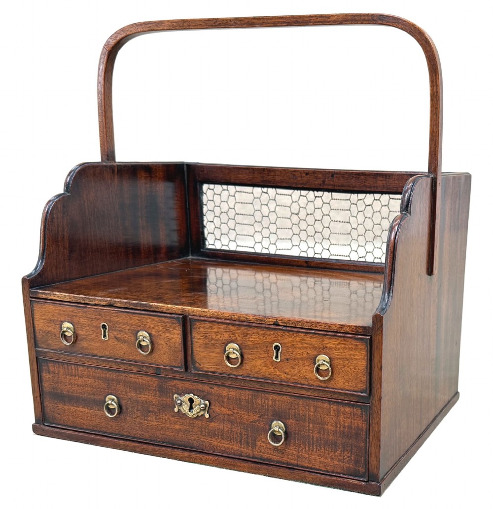 An 18th-century Georgian mahogany book carrier featuring a curved wooden top handle, a rear wire mesh panel, shaped side galleries, and three small drawers fitted with brass drop ring handles.