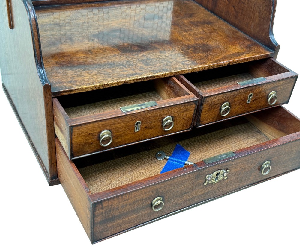 An 18th-century Georgian mahogany book carrier featuring a curved wooden top handle, a rear wire mesh panel, shaped side galleries, and three small drawers fitted with brass drop ring handles. View IV