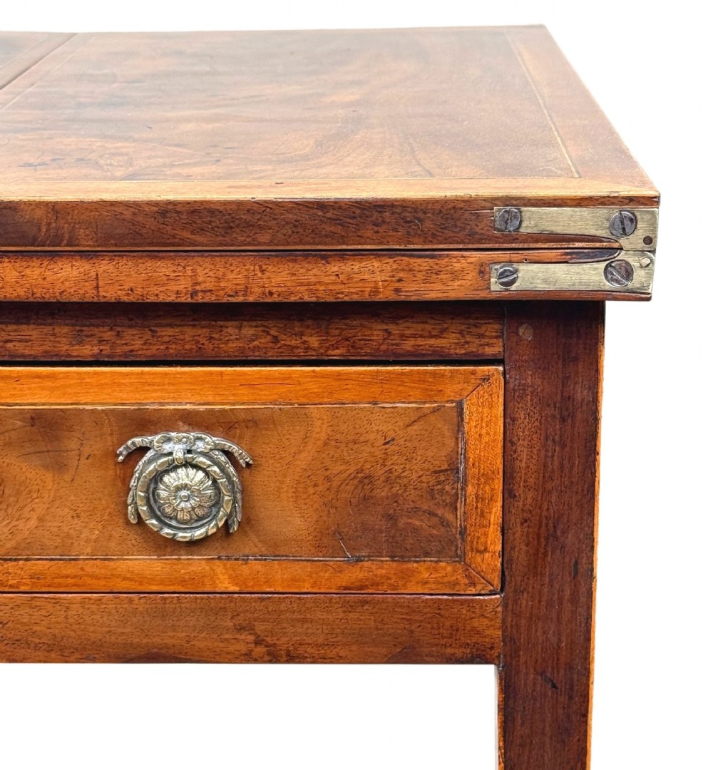 An 18th-century Georgian mahogany patience table featuring a folding top, brass corner brackets, a single drawer with ring handles, and square tapered legs. View VII