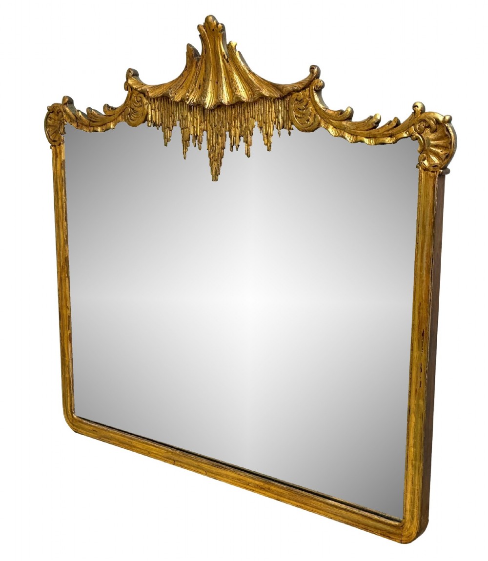 A late 19th-century giltwood wall mirror featuring a carved gesso cresting with scrollwork and dripping fringe details above a rectangular glass panel.