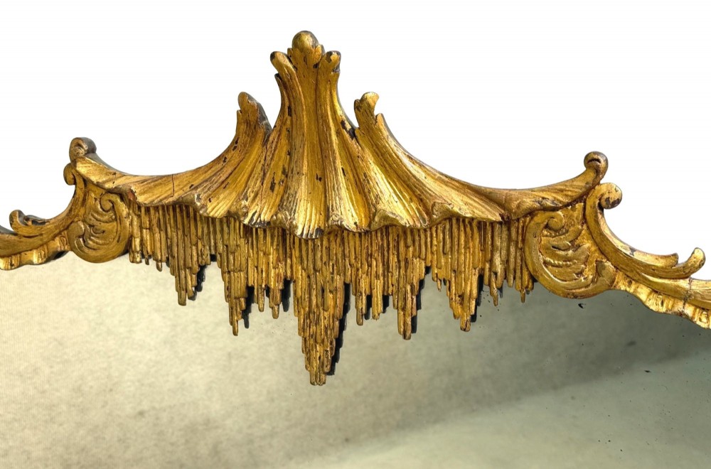 A late 19th-century giltwood wall mirror featuring a carved gesso cresting with scrollwork and dripping fringe details above a rectangular glass panel. View II