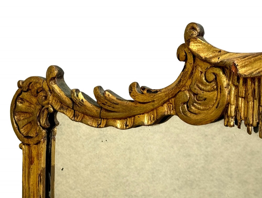 A late 19th-century giltwood wall mirror featuring a carved gesso cresting with scrollwork and dripping fringe details above a rectangular glass panel. View III