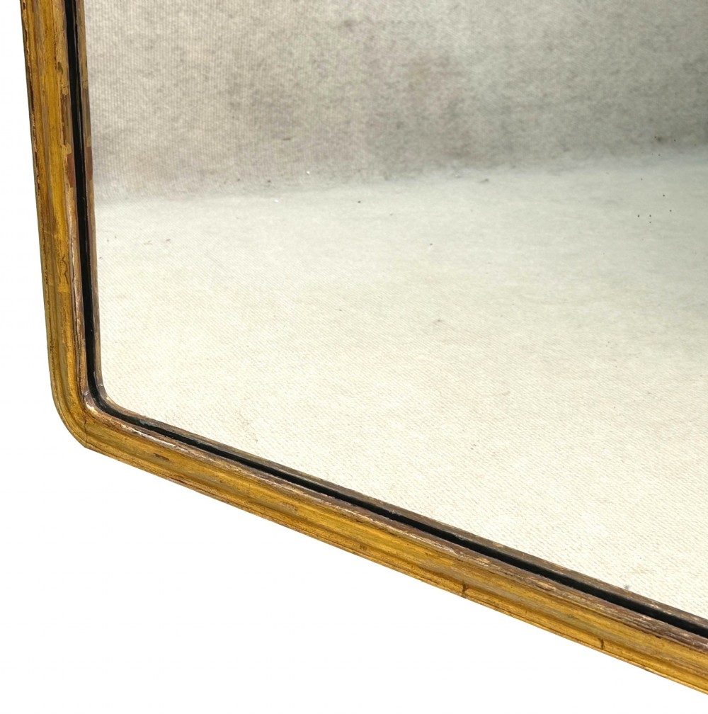 A late 19th-century giltwood wall mirror featuring a carved gesso cresting with scrollwork and dripping fringe details above a rectangular glass panel. View VII