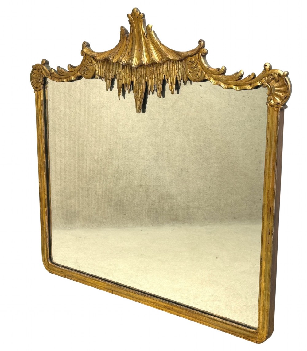 A late 19th-century giltwood wall mirror featuring a carved gesso cresting with scrollwork and dripping fringe details above a rectangular glass panel. View IX