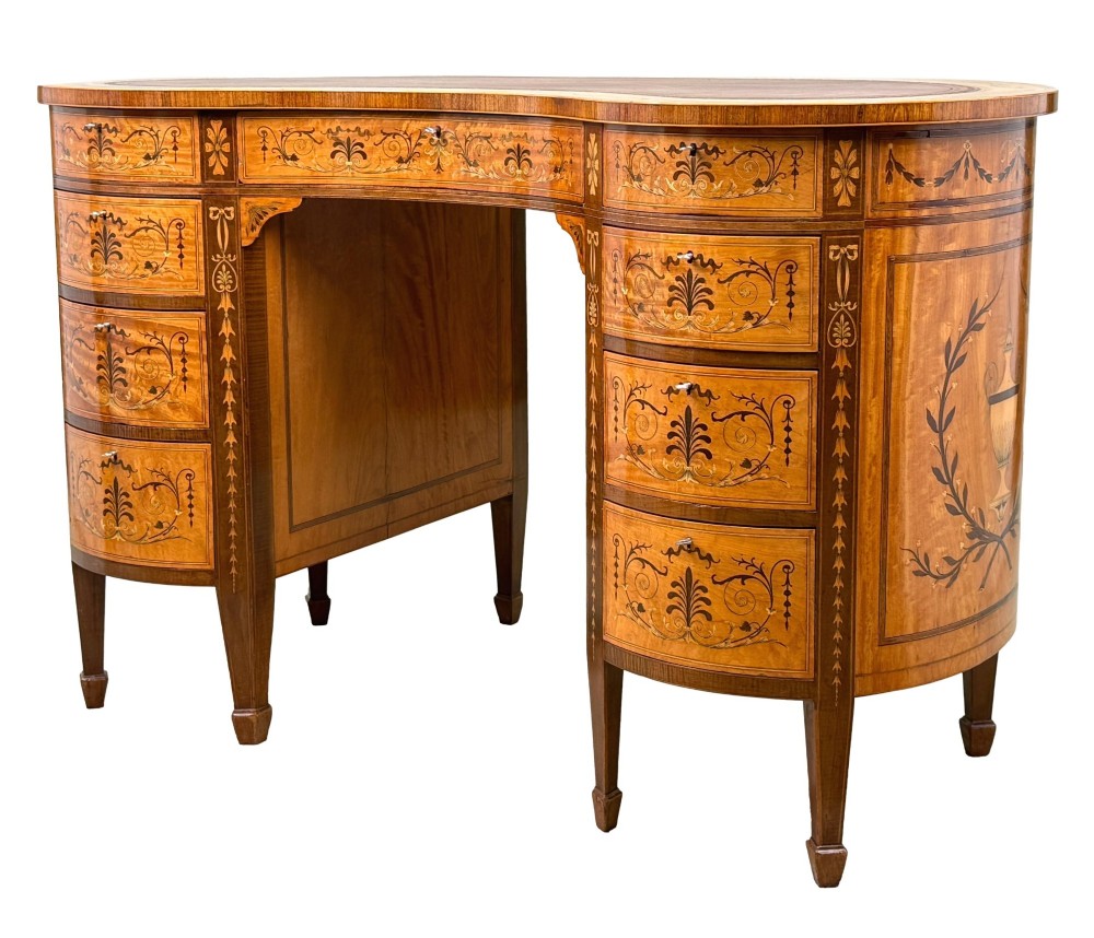 A late nineteenth-century kidney-shaped satinwood writing desk with detailed floral marquetry inlays, twin pedestals, and a leather insert top.