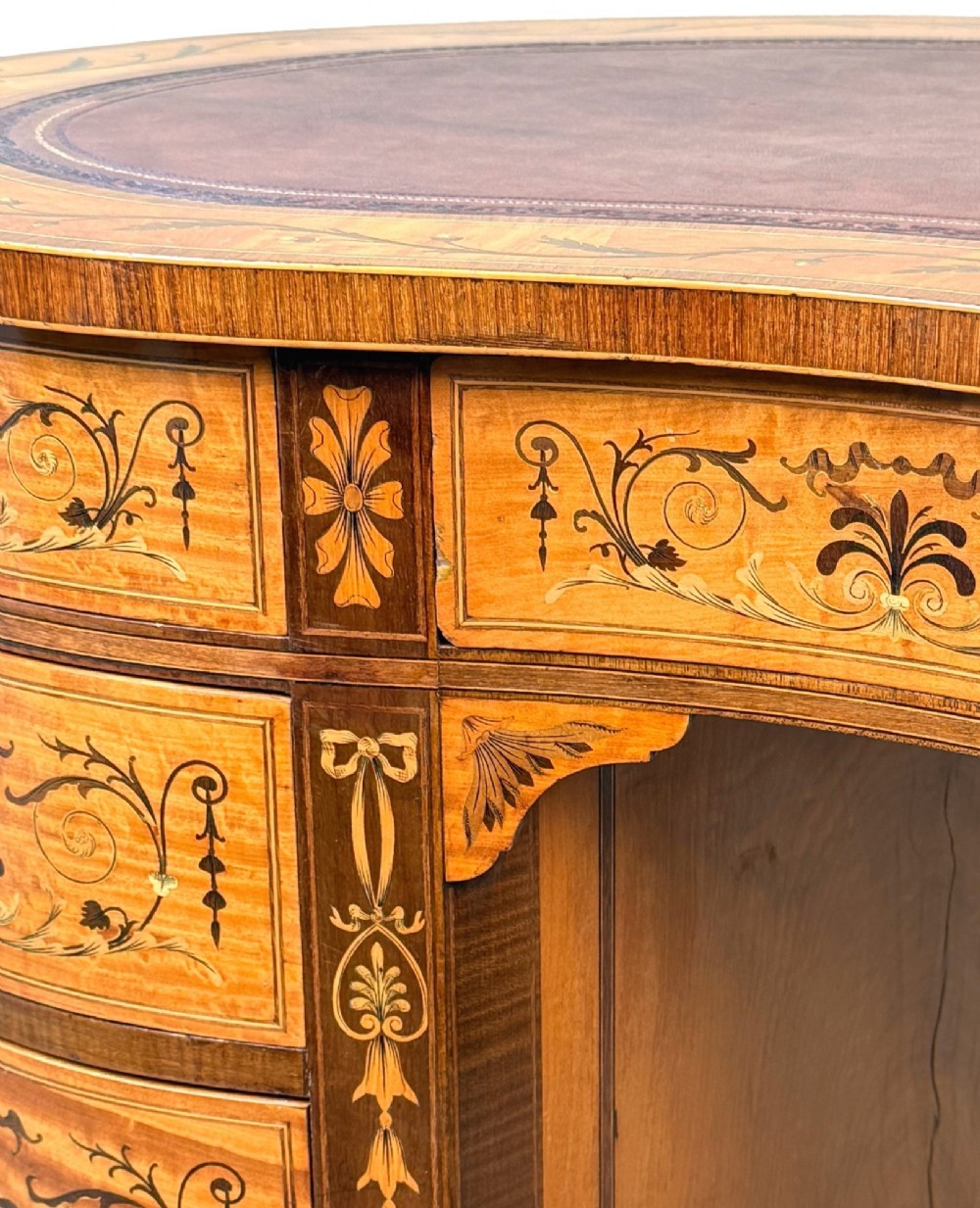 A late nineteenth-century kidney-shaped satinwood writing desk with detailed floral marquetry inlays, twin pedestals, and a leather insert top. View II