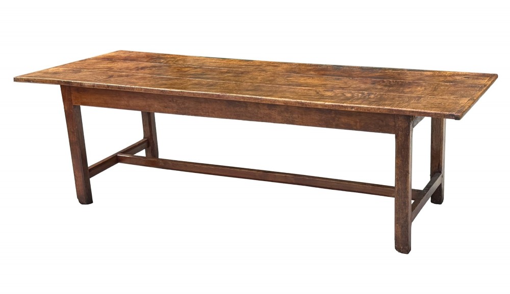An 18th-century English farmhouse dining table crafted from warm brown oak with a wide three-plank top, plain apron, and an H-stretcher base.