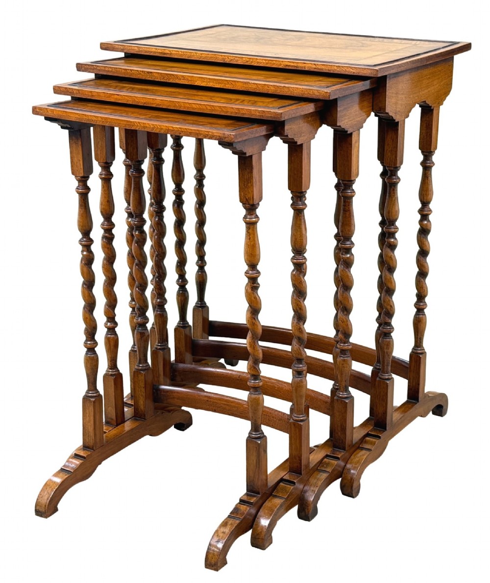 A set of four early twentieth-century brown walnut nesting tables featuring barley twist legs, arched stretchers, and banded inlaid tops stacked in graduated size.