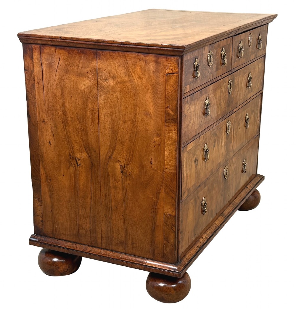 An early 18th-century Queen Anne walnut chest of drawers featuring figured grain veneers, brass drop handles, and turned bun feet. View II
