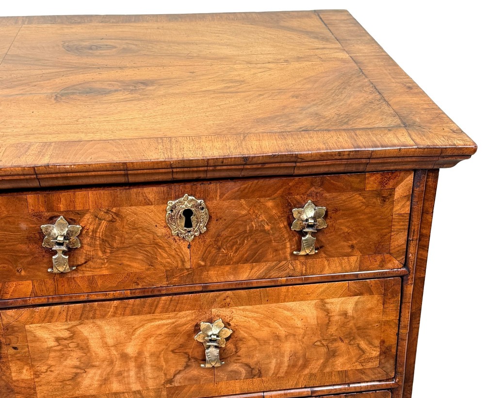 An early 18th-century Queen Anne walnut chest of drawers featuring figured grain veneers, brass drop handles, and turned bun feet. View III