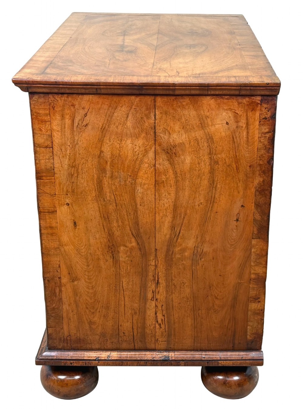 An early 18th-century Queen Anne walnut chest of drawers featuring figured grain veneers, brass drop handles, and turned bun feet. View V
