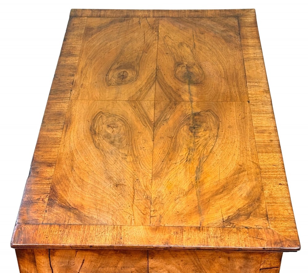 An early 18th-century Queen Anne walnut chest of drawers featuring figured grain veneers, brass drop handles, and turned bun feet. View VI