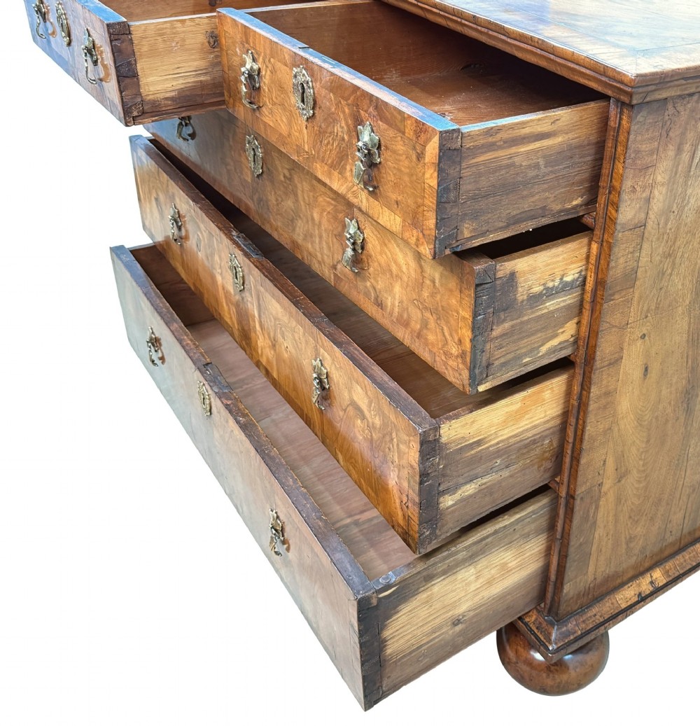An early 18th-century Queen Anne walnut chest of drawers featuring figured grain veneers, brass drop handles, and turned bun feet. View VIII