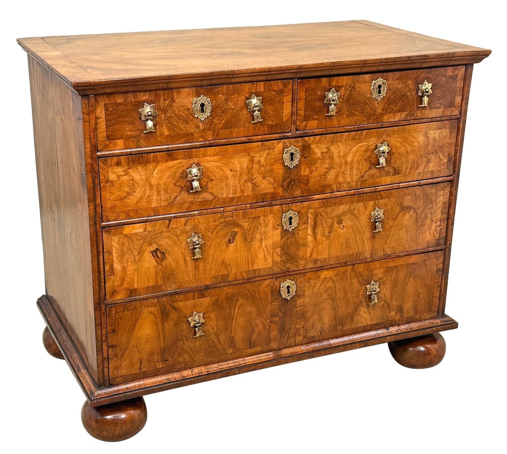 An early 18th-century Queen Anne walnut chest of drawers featuring figured grain veneers, brass drop handles, and turned bun feet. View IX