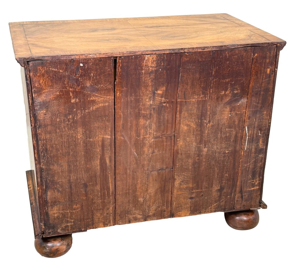 An early 18th-century Queen Anne walnut chest of drawers featuring figured grain veneers, brass drop handles, and turned bun feet. View X