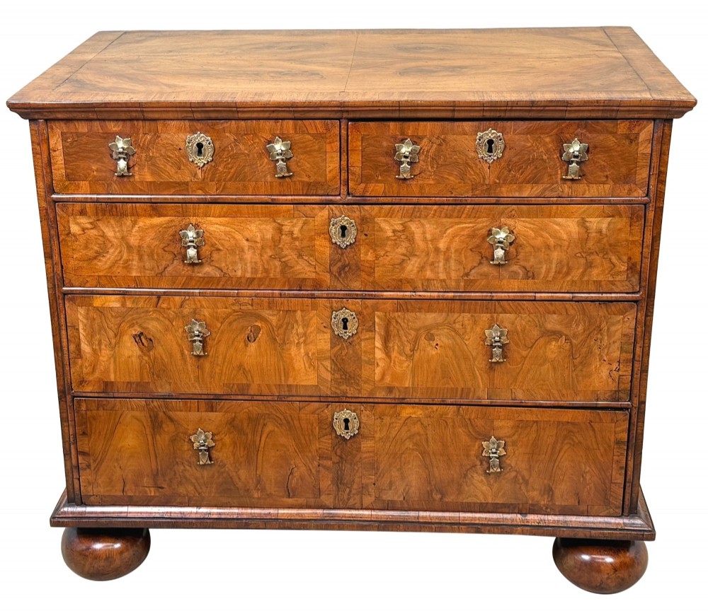 An early 18th-century Queen Anne walnut chest of drawers featuring figured grain veneers, brass drop handles, and turned bun feet. View XI