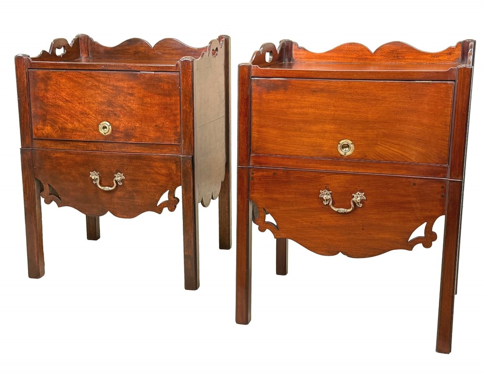 A matched pair of 18th-century Georgian mahogany bedside tables featuring scalloped tray top galleries, brass hardware, and shaped aprons.