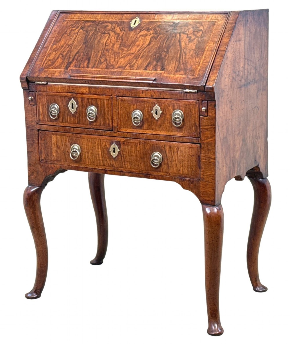 An early 18th-century walnut bureau on legs featuring a slant-front lid, small drawers with brass teardrop handles, and cabriole legs.