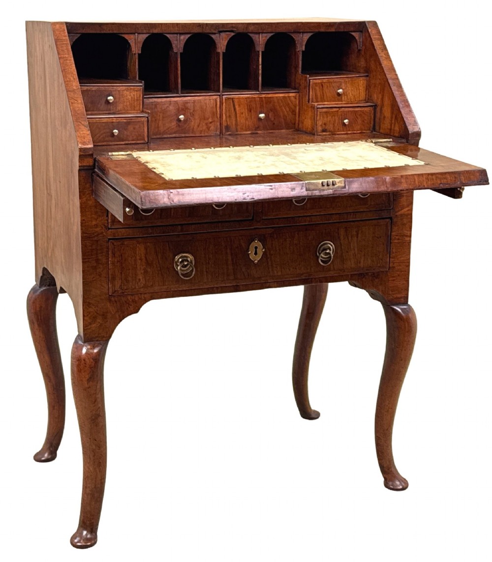 An early 18th-century walnut bureau on legs featuring a slant-front lid, small drawers with brass teardrop handles, and cabriole legs. View II