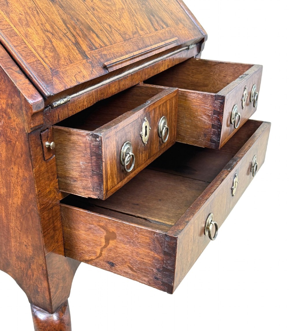 An early 18th-century walnut bureau on legs featuring a slant-front lid, small drawers with brass teardrop handles, and cabriole legs. View X