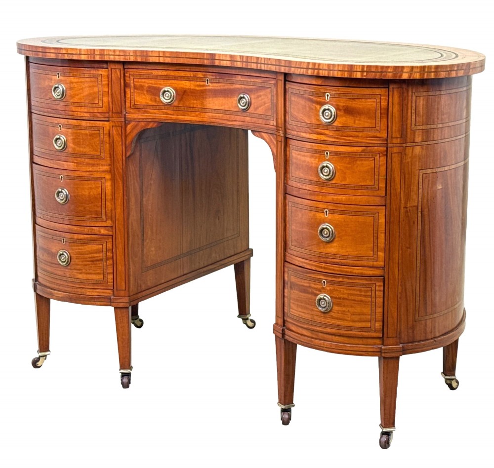 A 19th-century kidney-shaped satinwood writing desk featuring an inset green leather top, nine inlaid drawers with brass ring handles, and tapered square legs on castors.