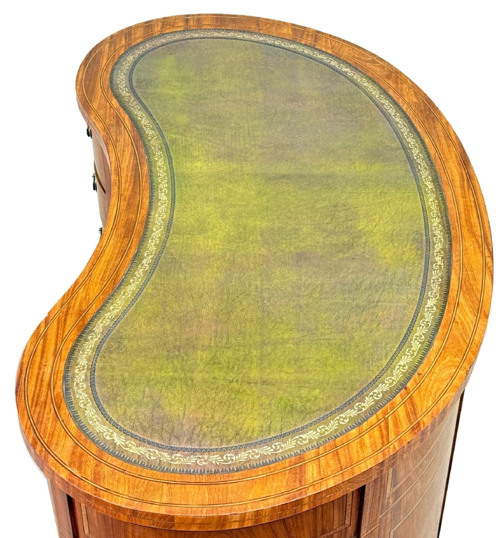 A 19th-century kidney-shaped satinwood writing desk featuring an inset green leather top, nine inlaid drawers with brass ring handles, and tapered square legs on castors. View II