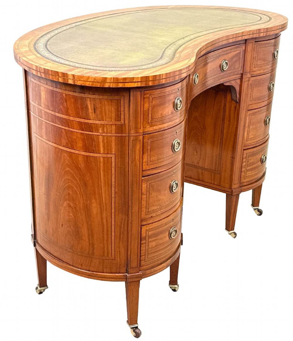 A 19th-century kidney-shaped satinwood writing desk featuring an inset green leather top, nine inlaid drawers with brass ring handles, and tapered square legs on castors. View III