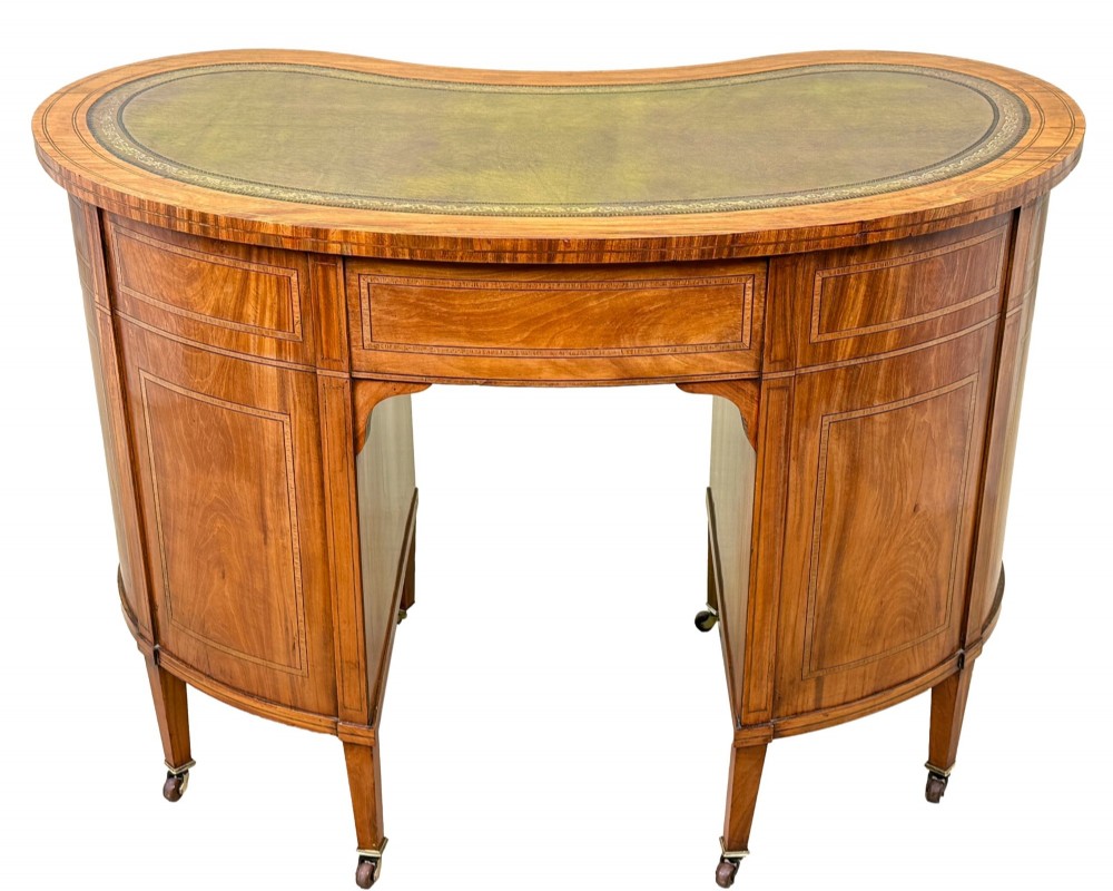 A 19th-century kidney-shaped satinwood writing desk featuring an inset green leather top, nine inlaid drawers with brass ring handles, and tapered square legs on castors. View IX