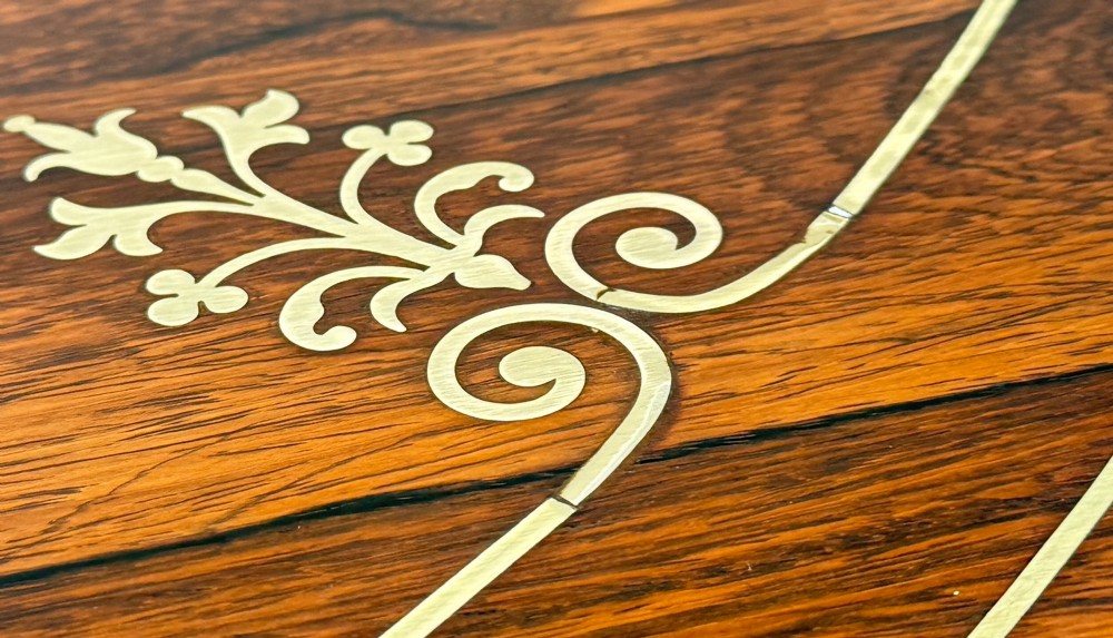 A circular Regency rosewood centre table featuring brass inlay motifs around the rim, a central pedestal support, and a quadform base with splayed legs ending in brass paw castors. View IV