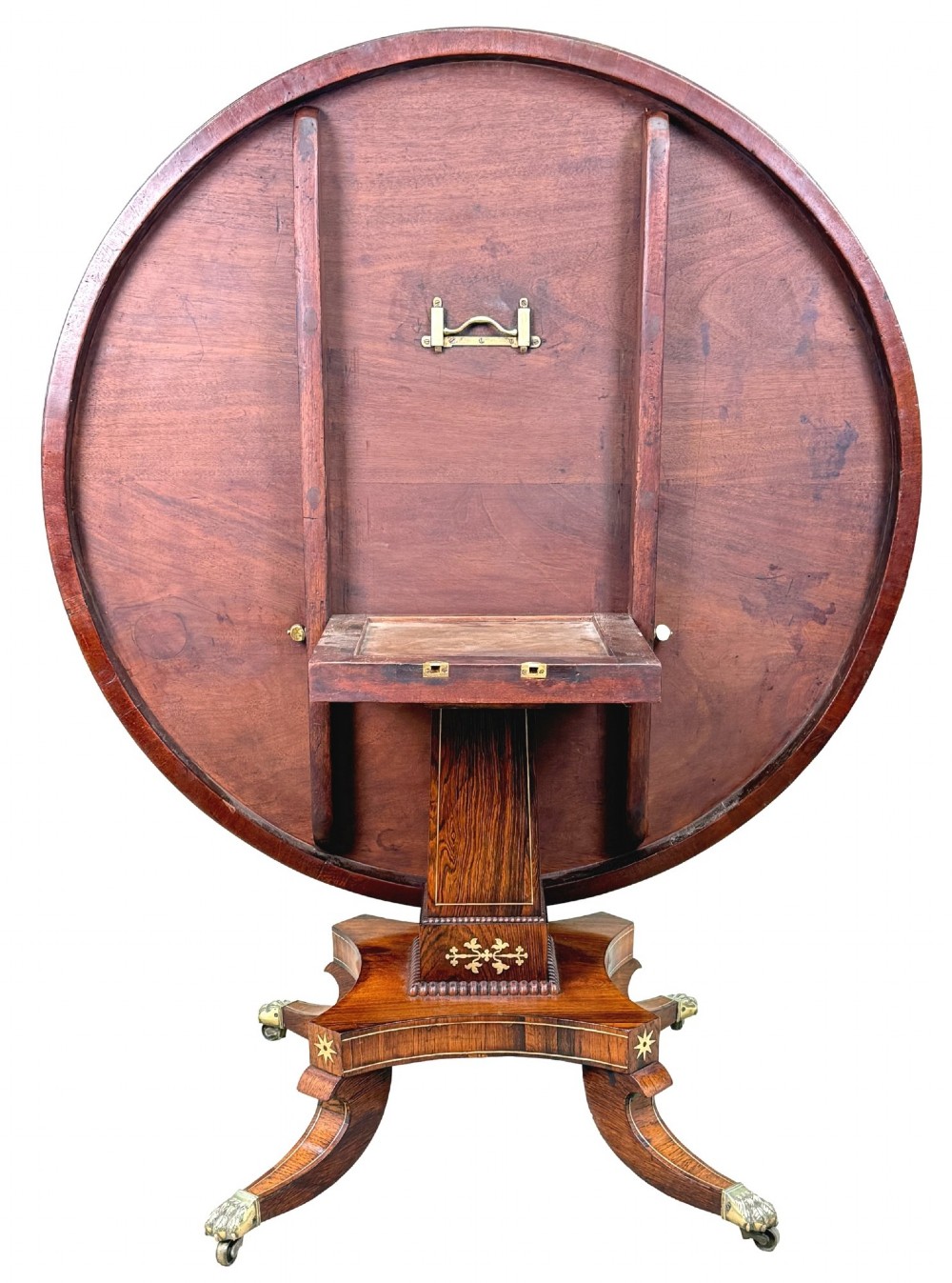 A circular Regency rosewood centre table featuring brass inlay motifs around the rim, a central pedestal support, and a quadform base with splayed legs ending in brass paw castors. View XII