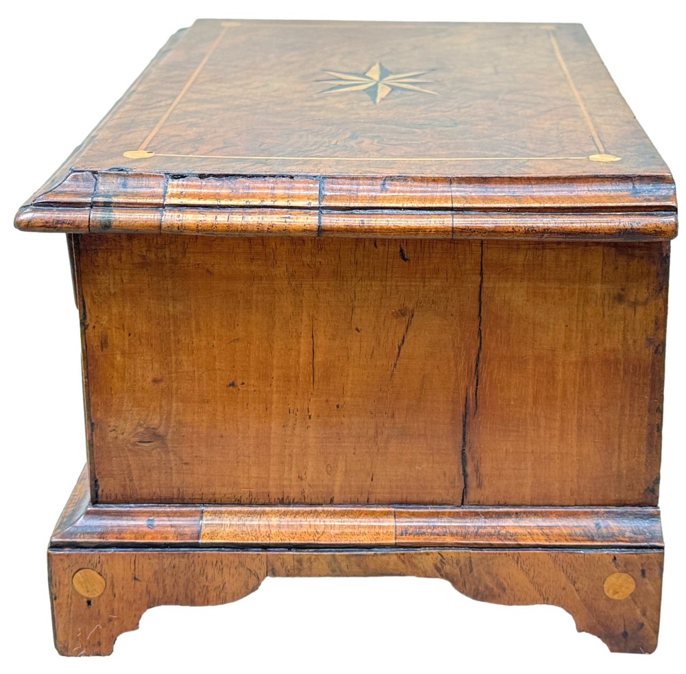 An early 18th-century walnut miniature chest featuring two drawers, star marquetry inlay, crossbanding, brass drop ring handles, and bracket feet. View III